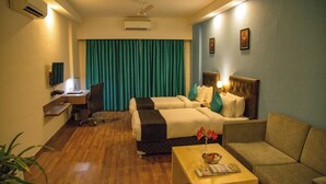 A hotel room with two beds, a desk, a chair, a sofa, a coffee table, and a ceiling fan. - Saramax Inn (Roorkee)