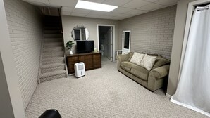Una habitación con una escalera, un televisor sobre un aparador de madera, un sofá y una puerta que da a otra estancia.