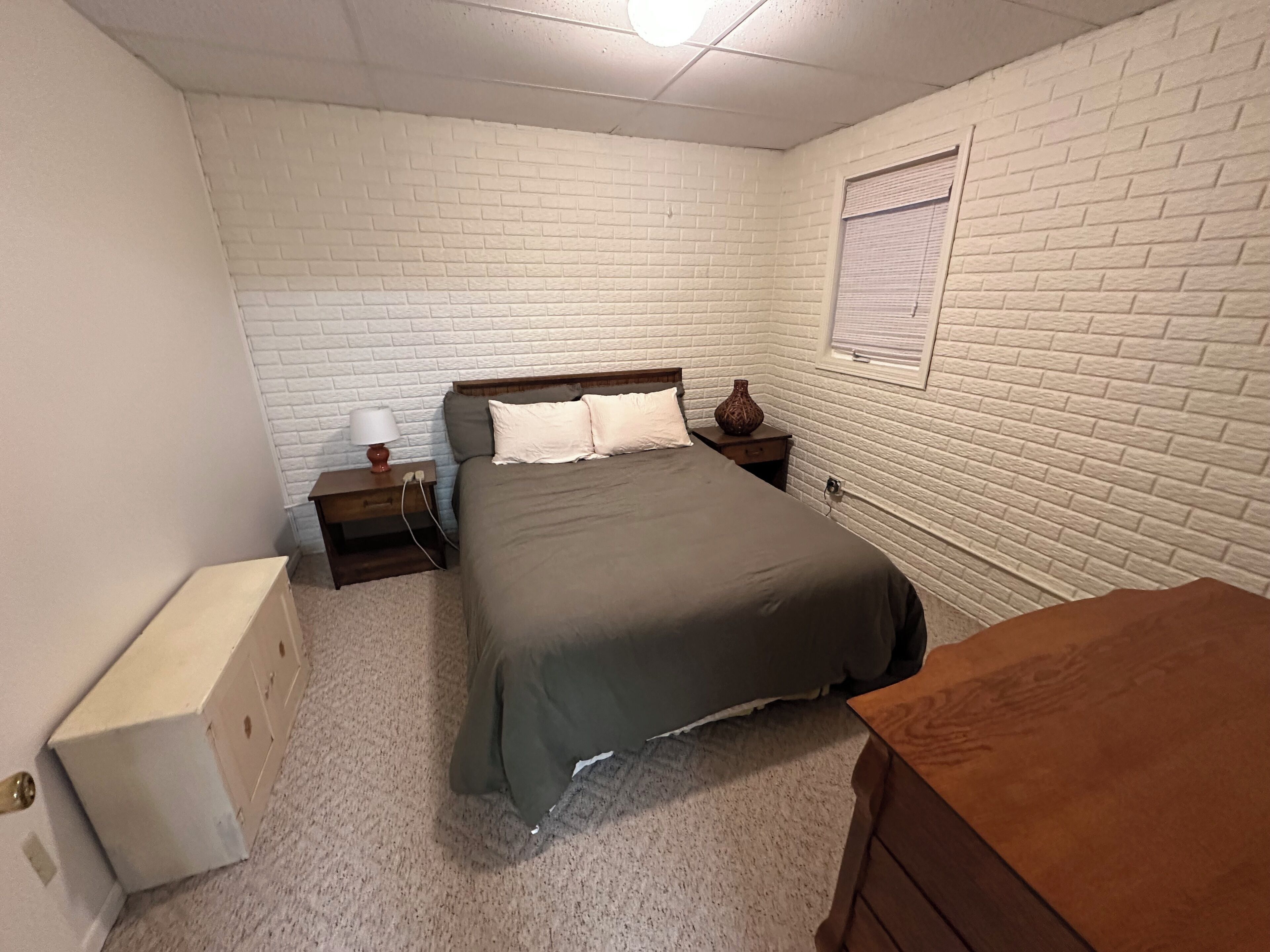 Une chambre à coucher avec un lit, des tables de chevet, une lampe, un vase et une fenêtre avec des stores.