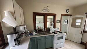 Una cocina con microondas, estufa, fregadero y armarios. Hay un reloj en la pared y un cartel con un mensaje.