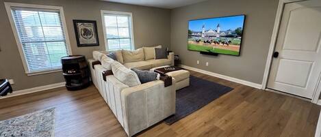 A living room with a sectional sofa, a flat-screen TV, and a wooden floor.