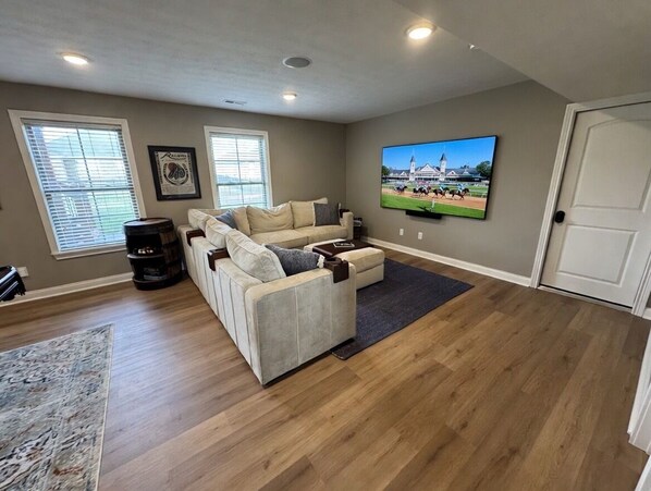 Ein Wohnzimmer mit einem Ecksofa, einem Flachbildfernseher und Holzboden.