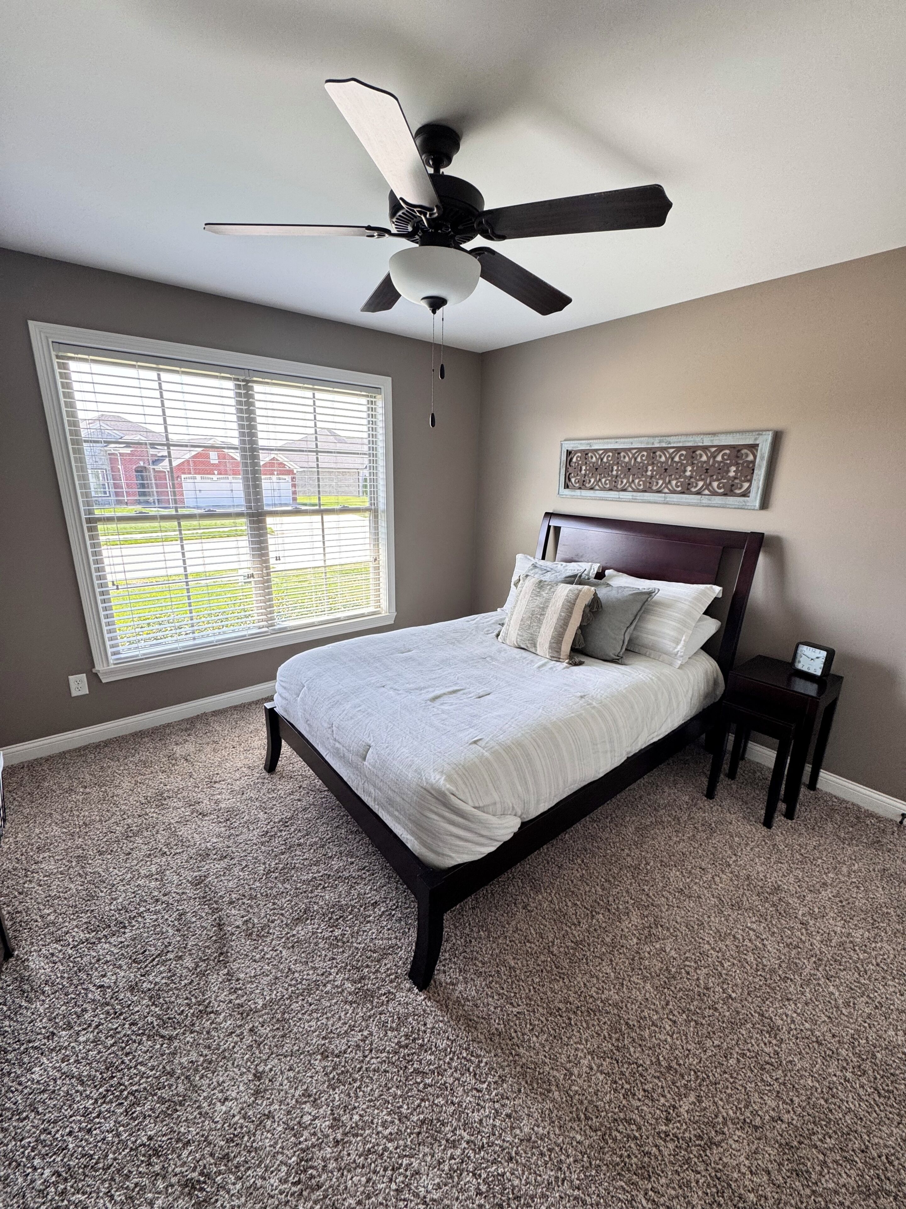 A bedroom with a bed, a ceiling fan, a window, and a wall clock.