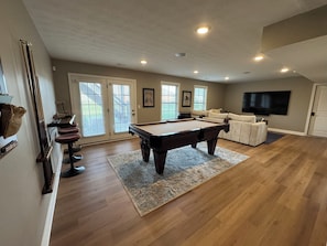 Uma sala de estar com mesa de bilhar, um sofá, uma televisão e uma porta com vista.