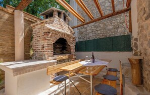 An outdoor brick oven with a table and benches, surrounded by stone walls and wooden beams. - Villa Ivana Heated& Saltwater Pool (Donji Vinjani)