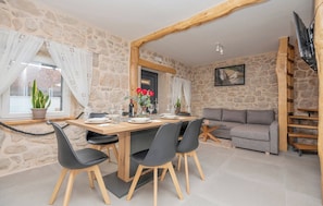 A stone-walled room with a wooden dining table, four chairs, a sofa, and a TV. - Villa Ivana Heated& Saltwater Pool (Donji Vinjani)