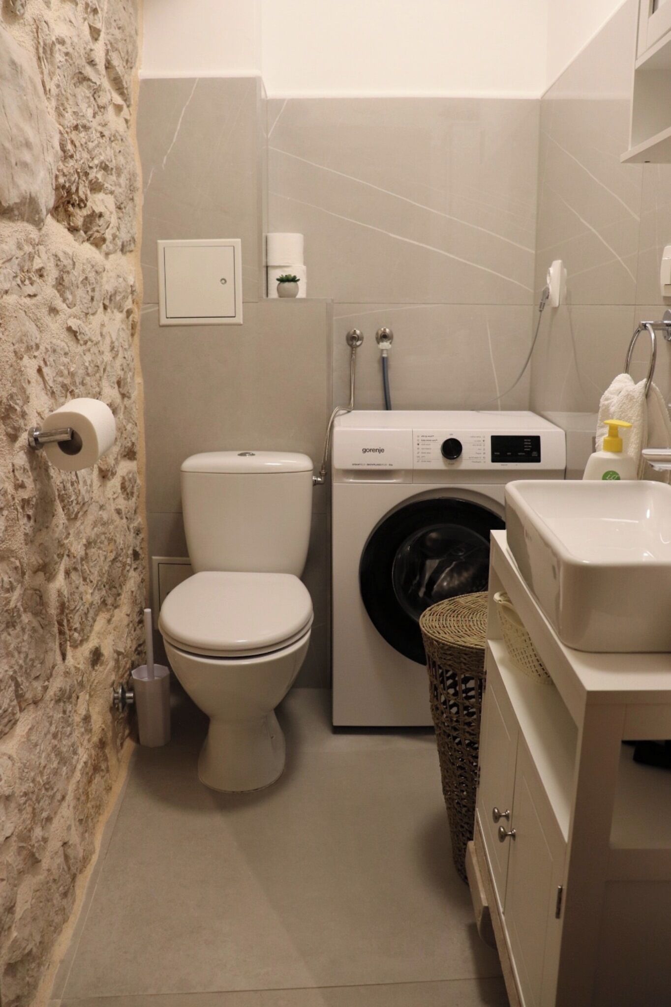 A compact bathroom with a toilet, washing machine, and sink.