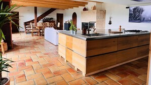 A spacious kitchen with a large island, wooden beams, and a fireplace. - Magnificent Villa with Panoramic Views & Pool (Fabras)