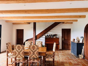 Un espace repas avec une table et des chaises en bois, un escalier et un piano.