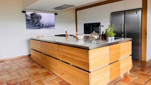 A modern kitchen with a large island, built-in appliances, and a large window with a tree view. - Magnificent Villa with Panoramic Views & Pool (Fabras)