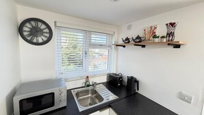 A kitchen with a microwave, sink, and window with blinds. - modern studio flat with free parking near tube (Ruislip)