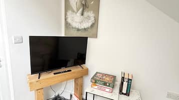 A room with a television on a wooden stand, a small table with books and a board game, and a painting on the wall.