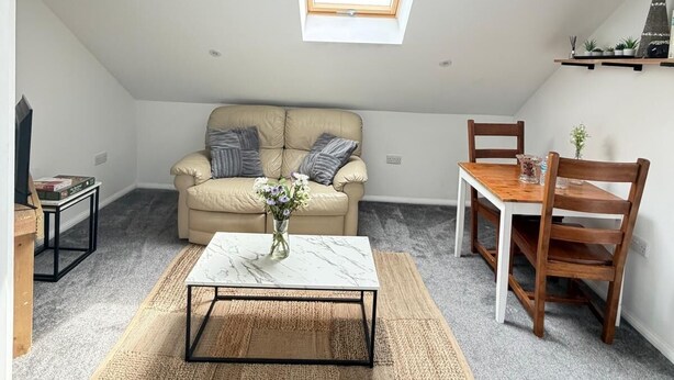A loft-style room with a skylight, a sofa, a coffee table, a dining table with chairs, and a small plant on the wall. - modern studio flat with free parking near tube (Ruislip)