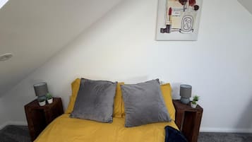 A bedroom with a sloped ceiling, a bed with yellow bedding, two grey pillows, and a framed picture on the wall.