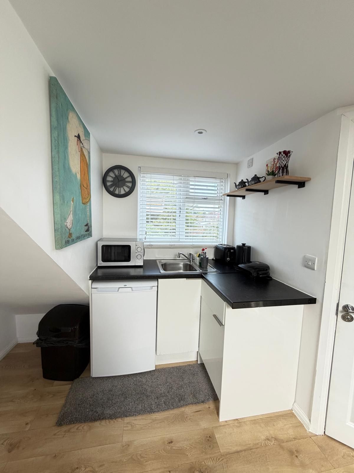 Een kleine keuken met een magnetron, spoelbak en een raam met zonwering.