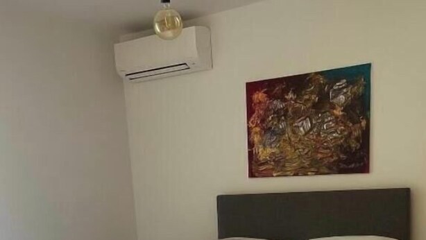 A neatly made bed with white linens and two rolled towels, an air conditioning unit, and a painting on the wall. - Ground-floor apartment in a quiet residence (Corte)