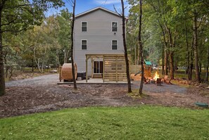 Ein zweistöckiges Haus mit überdachter Veranda und Feuerstelle im Garten.