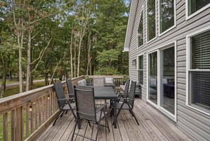 Eine Terrasse mit Gartenmöbeln, einem Holgitter und Blick auf Bäume sowie ein Haus.