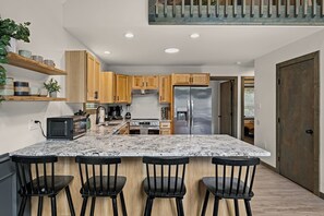 A modern kitchen with a large island, wooden cabinets, stainless steel appliances, and a built-in oven. - Stay & Play | Poconos Lake • Hot Tub • Sauna (Albrightsville)