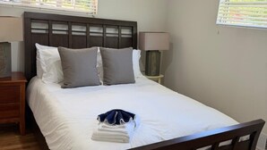 Une chambre à coucher avec un lit en bois, une literie blanche, une table de chevet avec une lampe et une fenêtre avec des stores.