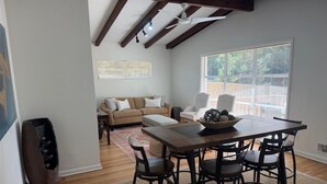 Un coin repas avec une table et des chaises en bois, un canapé et une fenêtre avec des stores.