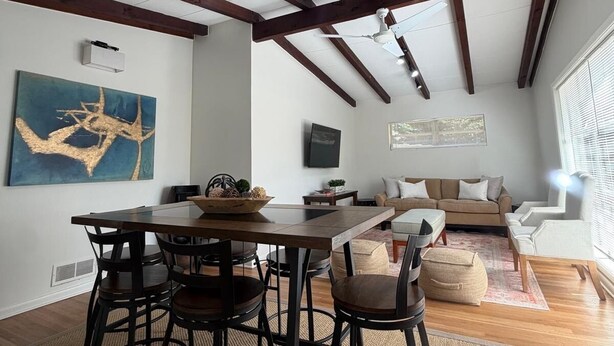 Un coin repas avec une table et des chaises en bois, un ventilateur de plafond et un grand tableau abstrait accroché au mur.
