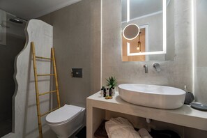 Ein Badezimmer mit einem weißen Waschbecken, einem Spiegel mit Beleuchtung, einer Toilette und einer Holzleiter.