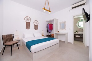 Ein Schlafzimmer mit einem Bett, einem Sessel, einem Schminktisch mit Spiegel und einem Traumfänger an der Wand.