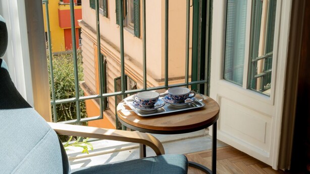 A balcony with a chair, a small table with a tray of dishes, and a view of a building with shutters. - TrastevereHome - Quiet 3 bedroom Home in Trastevere with Elevator (Rome)