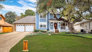 A two-story house with a front porch, garage, and a large tree in the yard. - Oak Canopy San Antonio Getaway (San Antonio)