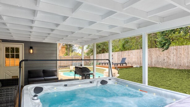 A covered outdoor area with a hot tub, seating, and a wooden fence in the background. - Oak Canopy San Antonio Getaway (San Antonio)