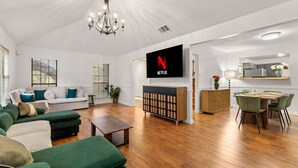 A modern living room with a flat-screen TV, green sofas, wooden flooring, and a dining area with a table and chairs. - Oak Canopy San Antonio Getaway (San Antonio)