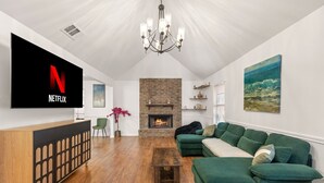 A living room with a Netflix TV, a fireplace, a green sofa, and a wooden coffee table. - Oak Canopy San Antonio Getaway (San Antonio)