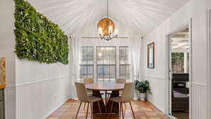 A dining area with a round table, four chairs, a chandelier, a large green wall, and a clock on the wall. - Oak Canopy San Antonio Getaway (San Antonio)