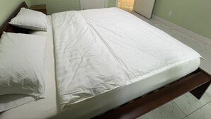 Cama com roupa de cama branca, cabeceira de madeira e pé de cama de madeira.