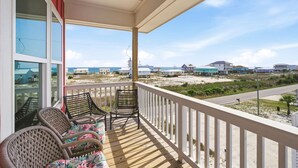 A balcony with wicker chairs and a view of a beach and houses. - Grenadine Dreams (Gulf Shores)