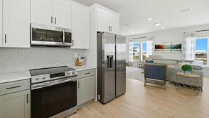 A modern kitchen with stainless steel appliances, white cabinetry, and a dining area with a sofa and a small round table. - Grenadine Dreams (Gulf Shores)