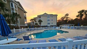 A pool area with blue lounge chairs and umbrellas, surrounded by a white fence. - Sea Bound | Golf Getaway + Pool | Myrtle Beach (Myrtle Beach)