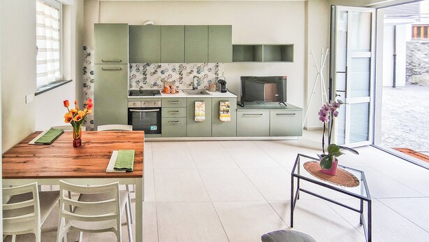 A modern kitchen with green cabinets, a dining area with a wooden table and white chairs, and a small side table with a potted plant. -  Casa Cavour - In Val di Susa con Parcheggio Moto (Bruzolo)
