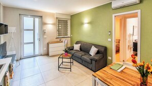 A modern living room with a sofa, a coffee table, and a dining table. There is a TV on a stand and a plant on the coffee table. -  Casa Cavour - In Val di Susa con Parcheggio Moto (Bruzolo)
