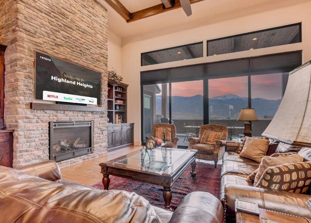 A spacious living room with a stone fireplace, leather furniture, and large windows offering a mountain view.