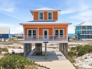 Ein zweistöckiges Strandhaus mit Balkon und einer Treppe, die zu der oberen Ebene führt, mit Blick auf das Meer.