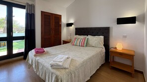 Een slaapkamer met een bed, nachtkastje, lamp, raam met gordijnen en een deur.