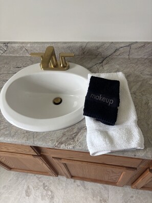 A bathroom sink with a gold faucet, a white towel, and a black towel with 'makeup' on it.