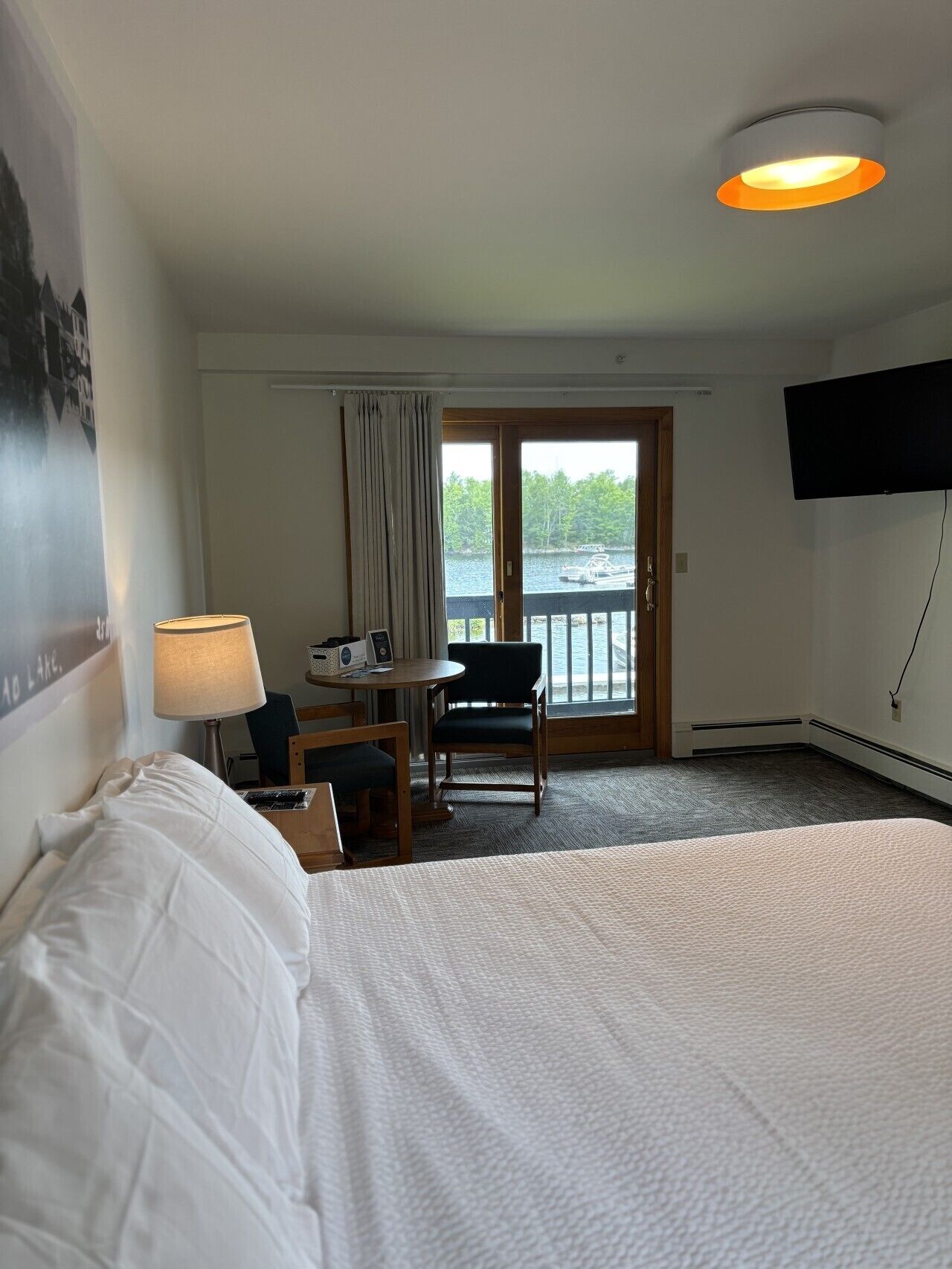 A hotel room with a bed, a desk, a chair, a TV, and a view of a lake.