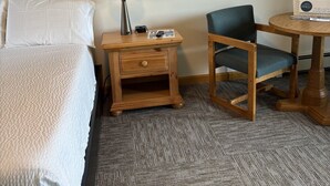 A hotel room with a bed, a nightstand, a lamp, a chair, and a small table with a box on it. - Juniper Motel*King*RM15*Dock*ATV Access*Waterfront*Kayak/Boat Rentals (Greenville)