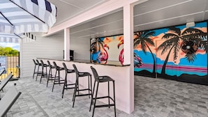 A bar area with a counter, black bar stools, and a mural with tropical and flamingo designs. - Marina Anne Monroe | Cool Mint Boutique Suite (Port Saint Joe)