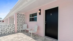 A pink building with a black door marked with the number 3, a white bench, and a decorative white fence. - Marina Anne Monroe | Cool Mint Boutique Suite (Port Saint Joe)