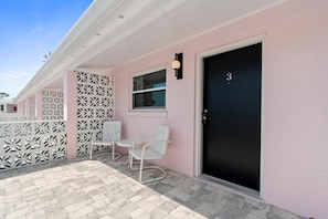 Un edificio rosa con una puerta negra marcada con el número 3, un banco blanco y una cerca decorativa blanca.