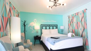 A bedroom with a bed, two bedside tables, a chair, a lamp, and a wall with a name. - Marina Anne Monroe | Cool Mint Boutique Suite (Port Saint Joe)